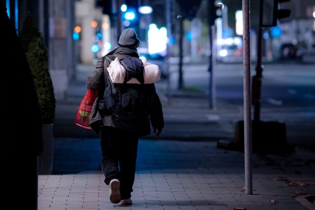 Photograph of a homeless person walking away from the camera down a street at night